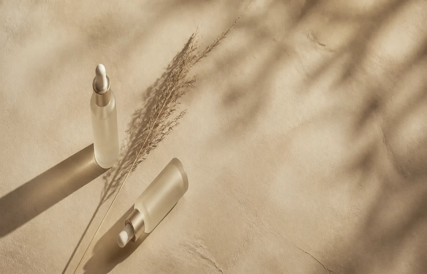 Two frosted glass dropper bottles and a dried grass stem on a slate blue stone slab