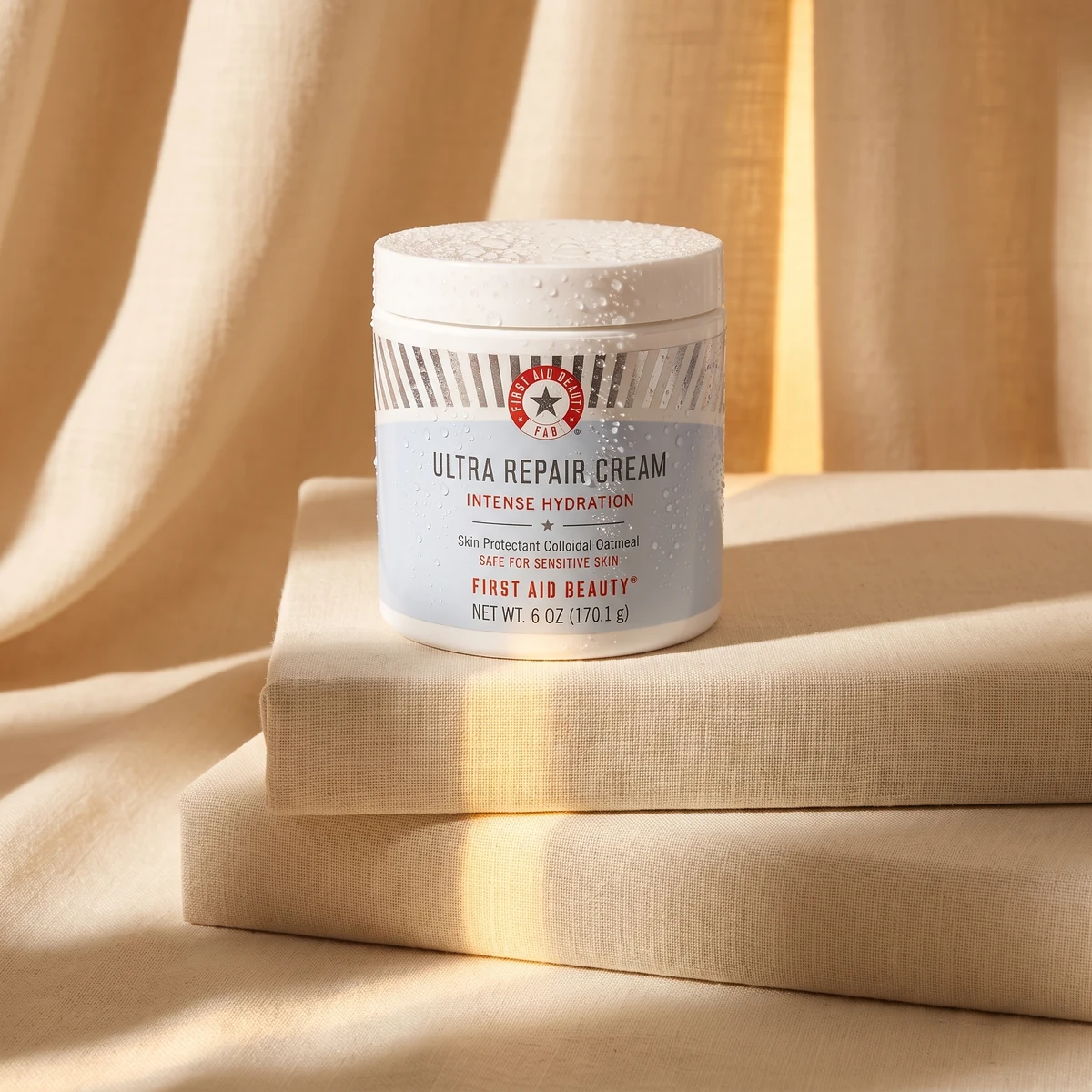 First Aid Beauty Ultra Repair Cream jar on warm stone, with a white lid and a red mark
