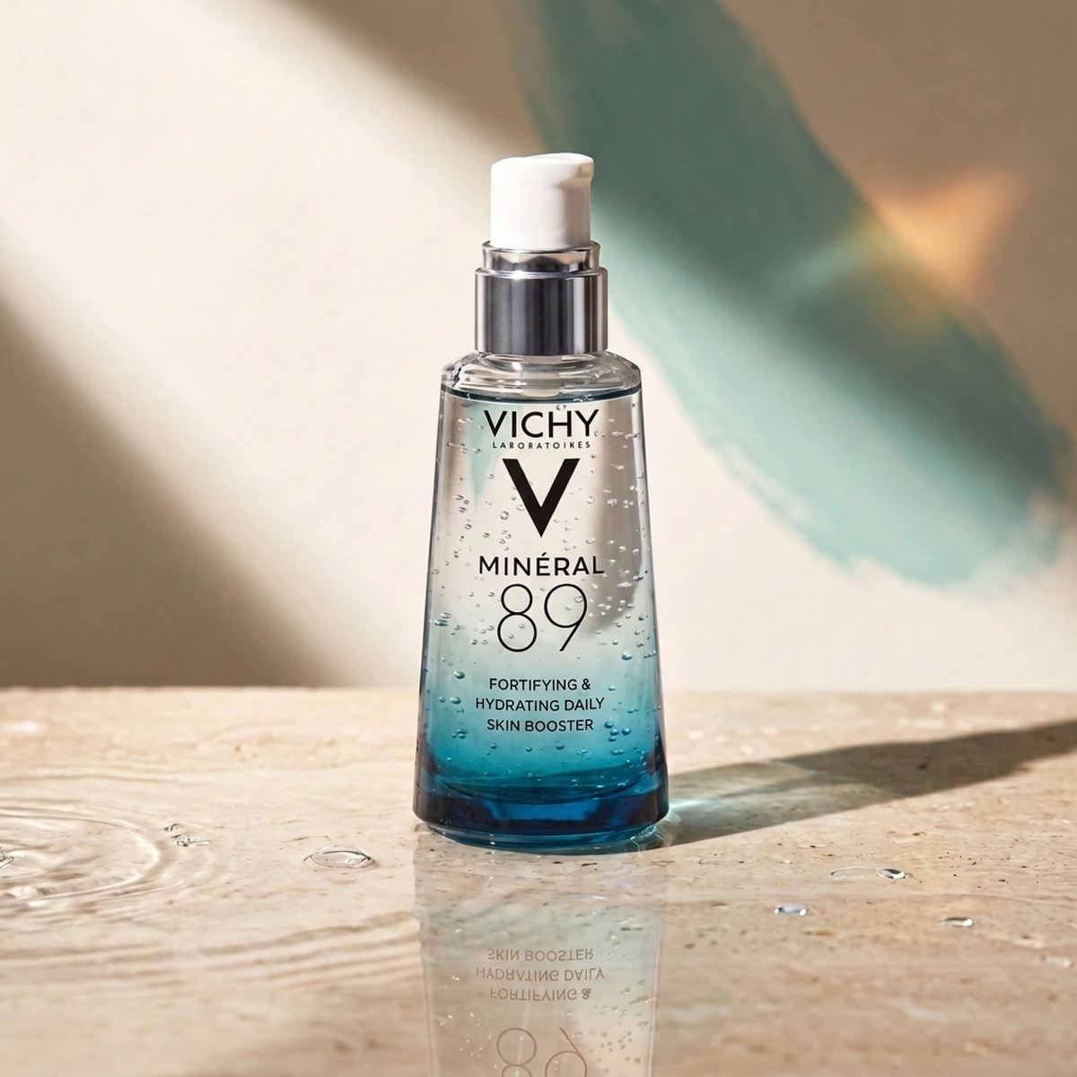 Vichy Minéral 89 glass pump bottle on wet stone, with water droplets and a soft teal wash behind it